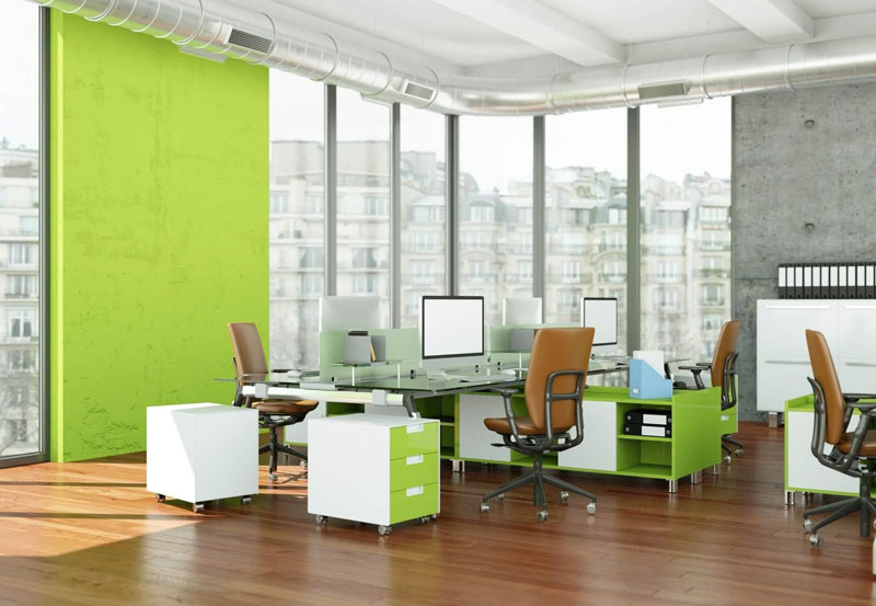 Wnętrze pokoju biurowego w przeszklonym biurowcu; kilkustanowiskowy szklany blat, obok kontenery biurowe i niskie komody na dokumenty w kolorze biało-limonkowym.