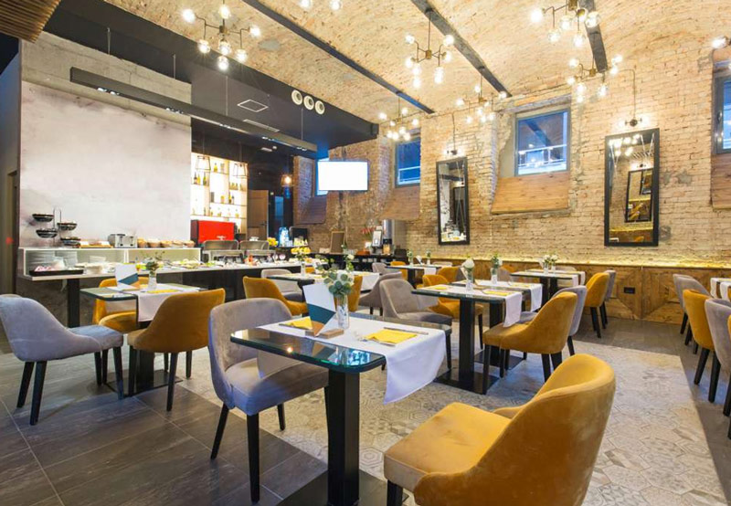 Restauracja w surowym, fabrycznym klimacie, który ocieplają zgrabne, tapicerowane krzesła w kolorze miodu i szarości